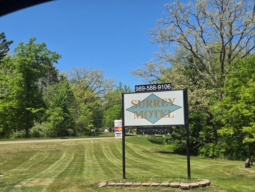 A roadside motel sign with phone number displayed in front of a landscaped property with green grass and trees on a clear day